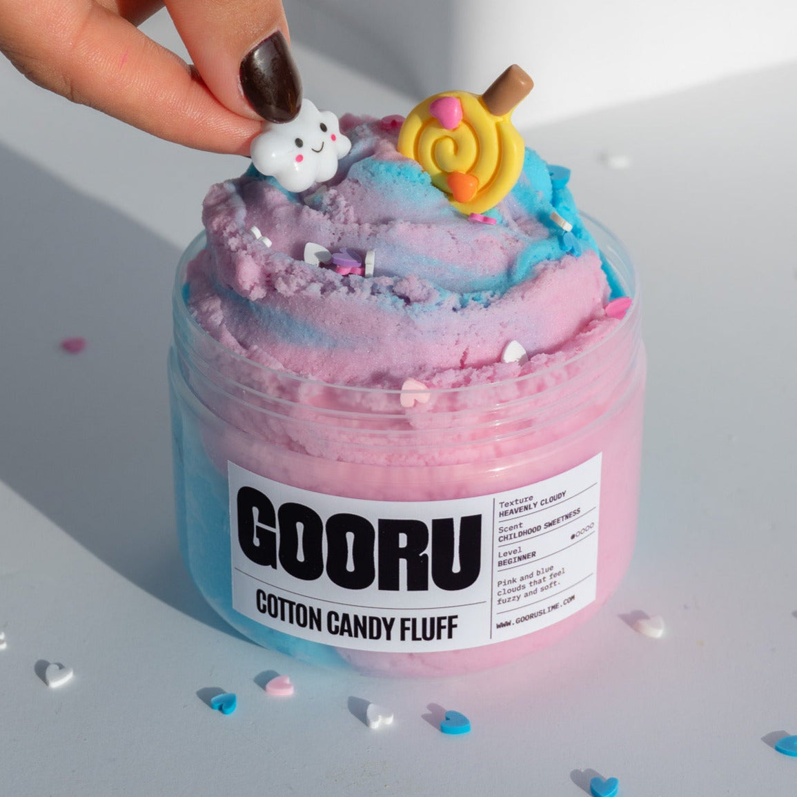A hand placing a smiling cloud charm onto the Cotton Candy Fluff slime, emphasizing the fluffy pastel texture and whimsical design.
