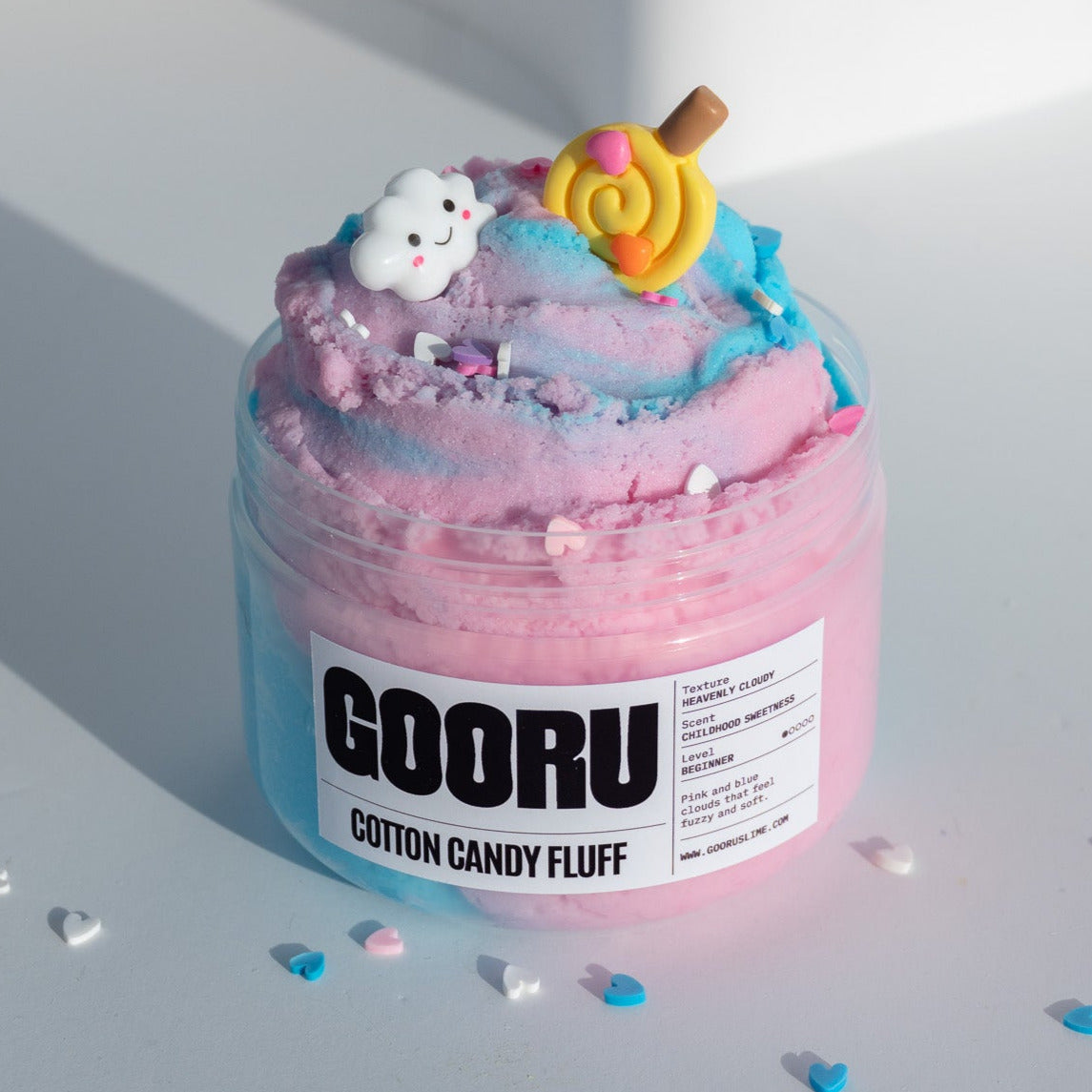 A jar of Cotton Candy Fluff slime featuring a dreamy pink and blue cloud texture, topped with a smiling cloud charm and a lollipop decoration.