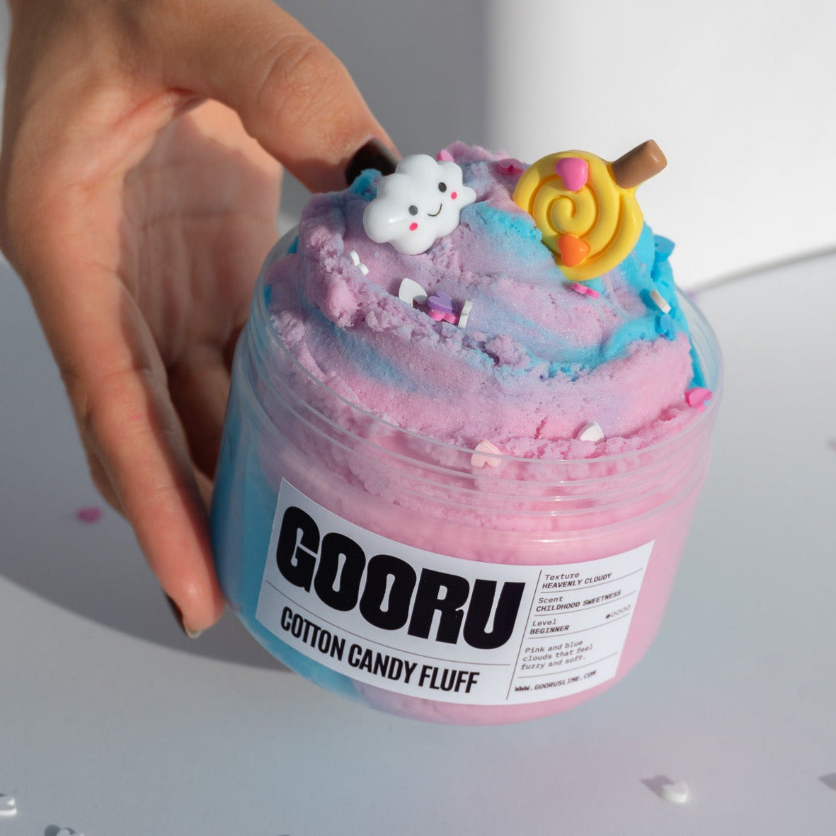 A hand gently holding the Cotton Candy Fluff slime jar, showcasing its dreamy design, complete with pastel swirls and playful decorations.