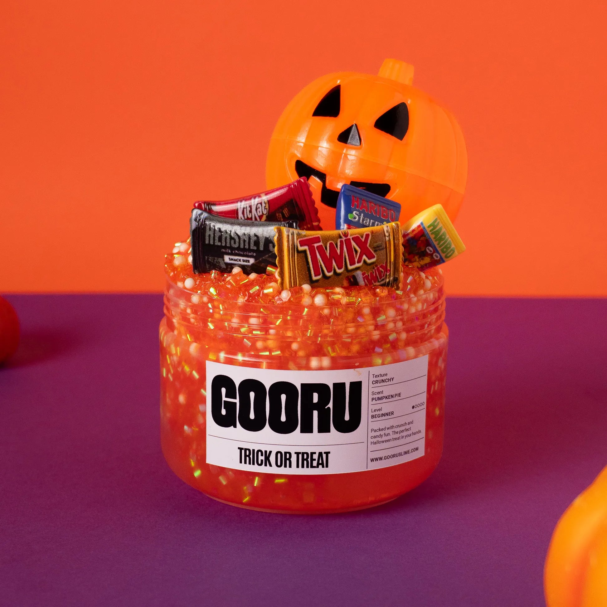 Jar of Halloween-themed candy with a pumpkin and candy bars on an orange and purple background.