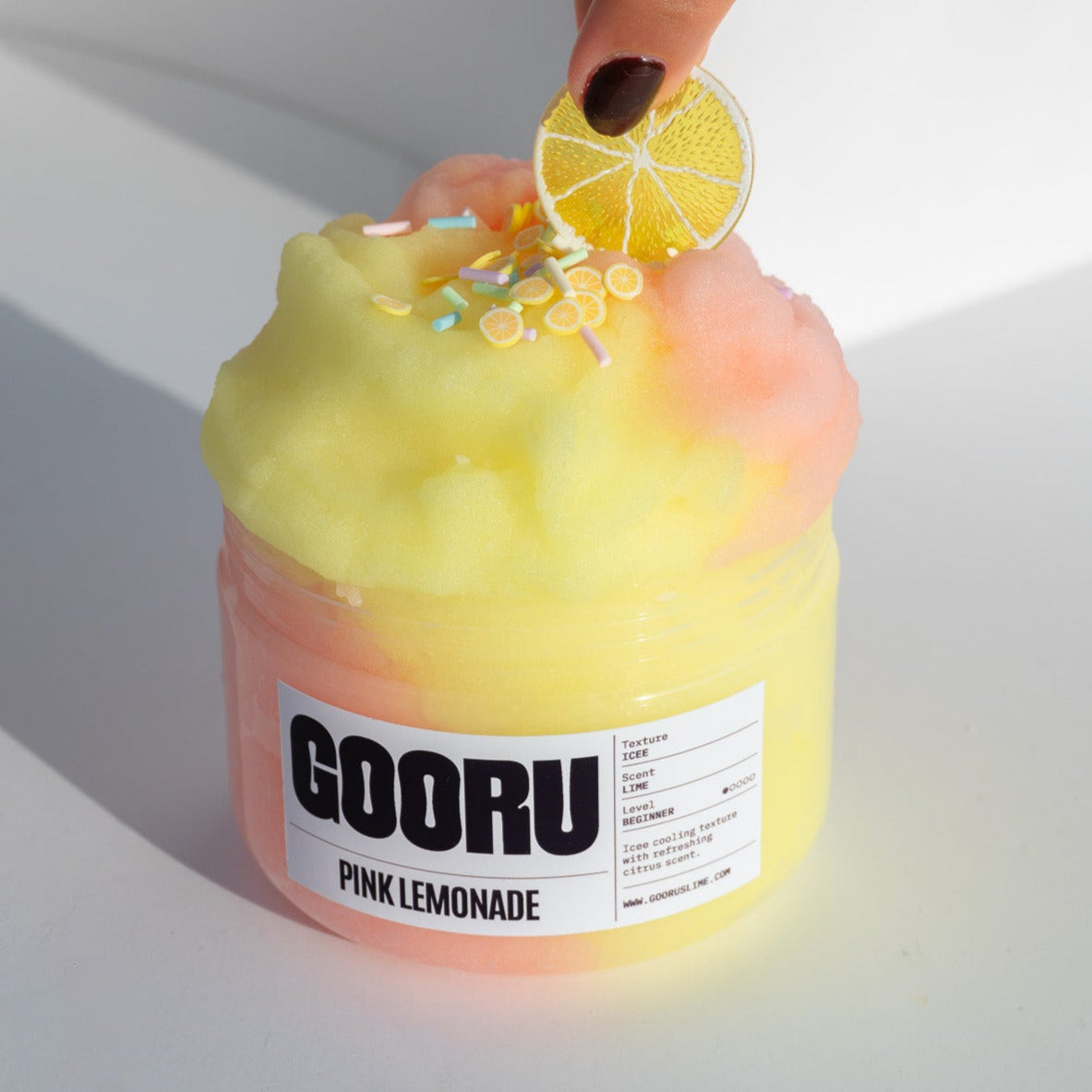 A hand adjusting the lemon slice charm on the Pink Lemonade slime, emphasizing its icy texture and citrusy details.