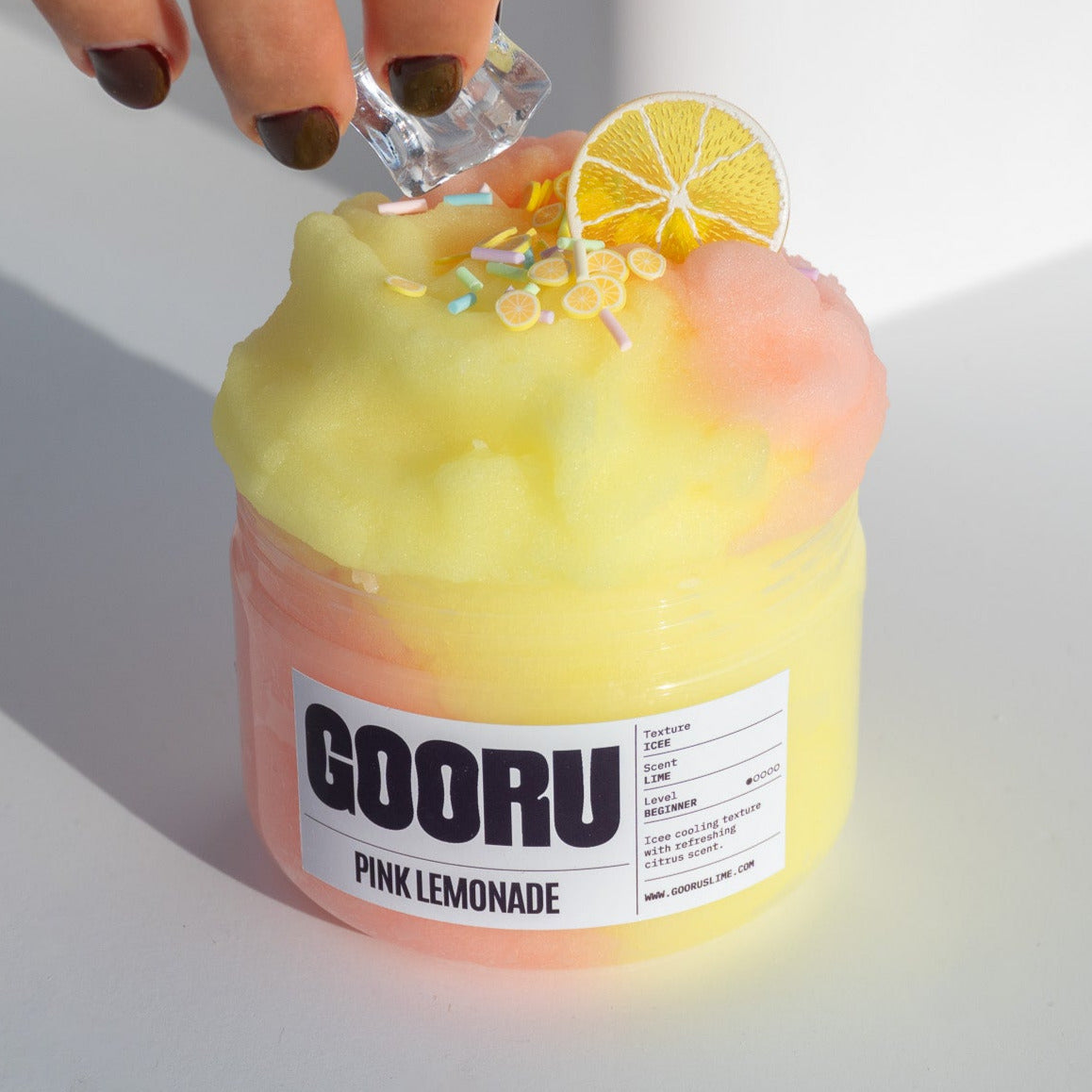 A hand placing an ice cube charm onto the Pink Lemonade slime jar, highlighting the refreshing citrus-themed design.