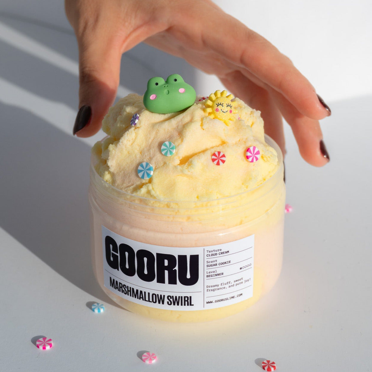  A hand holding the Marshmallow Swirl slime jar, emphasizing its soft texture and whimsical decorations, set against a clean background.