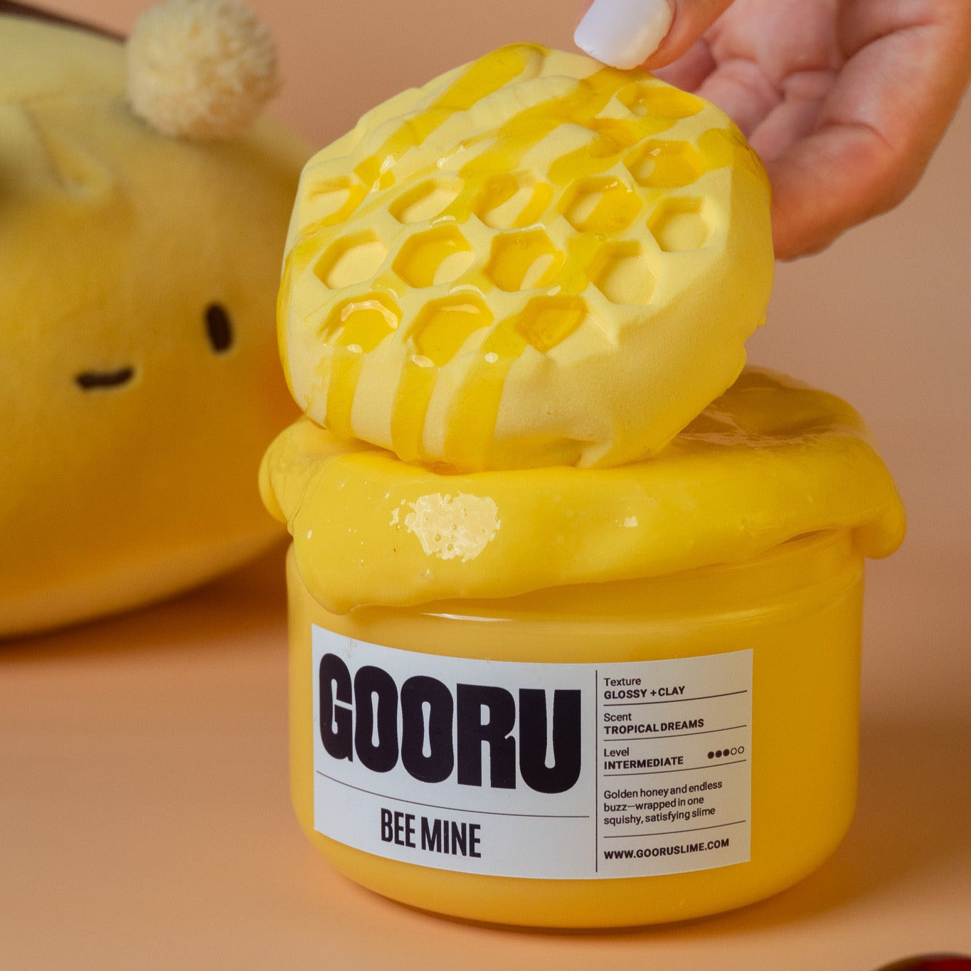 Hand placing honeycomb-shaped slime piece on top of the jar, with the “GOORU BEE MINE” label visible.