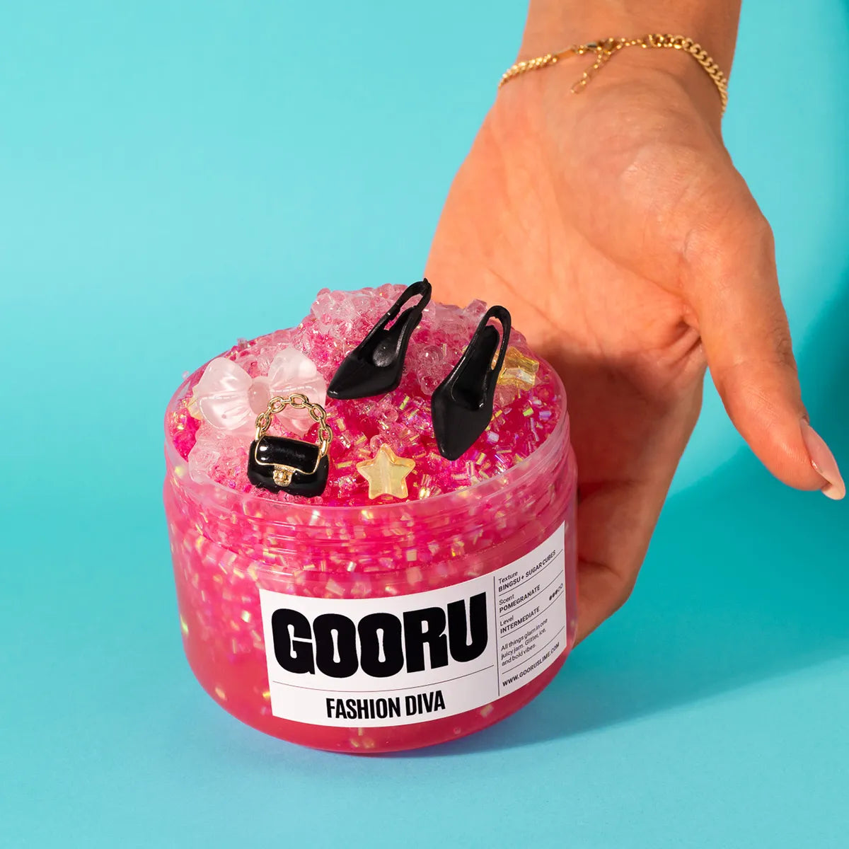 Pink slime container with black high heels and a small handbag, labeled 'GOORU Fashion Diva', held by a hand against a blue background.