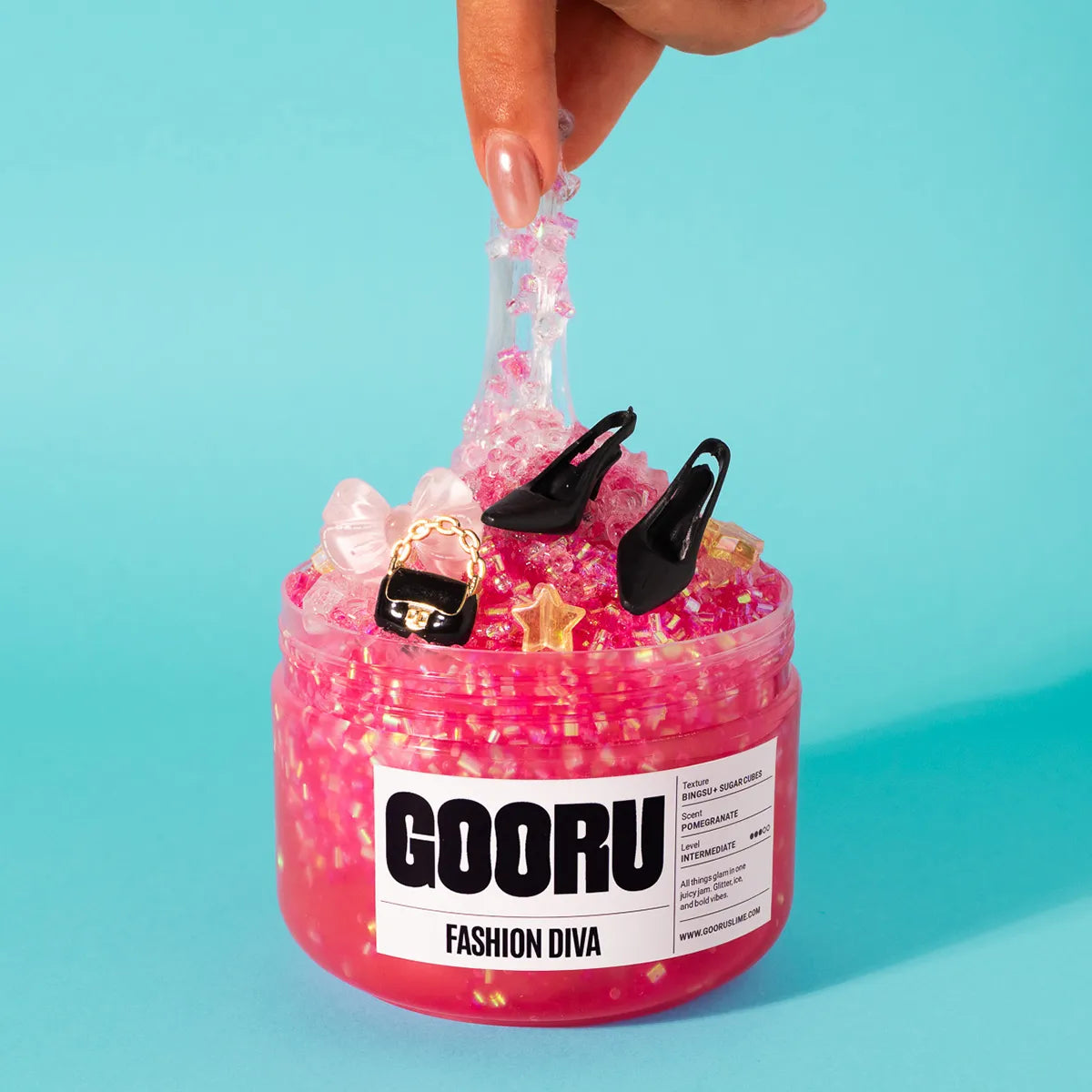 Pink slime jar labeled 'GOORU Fashion Diva'  with decorative items on a light blue background