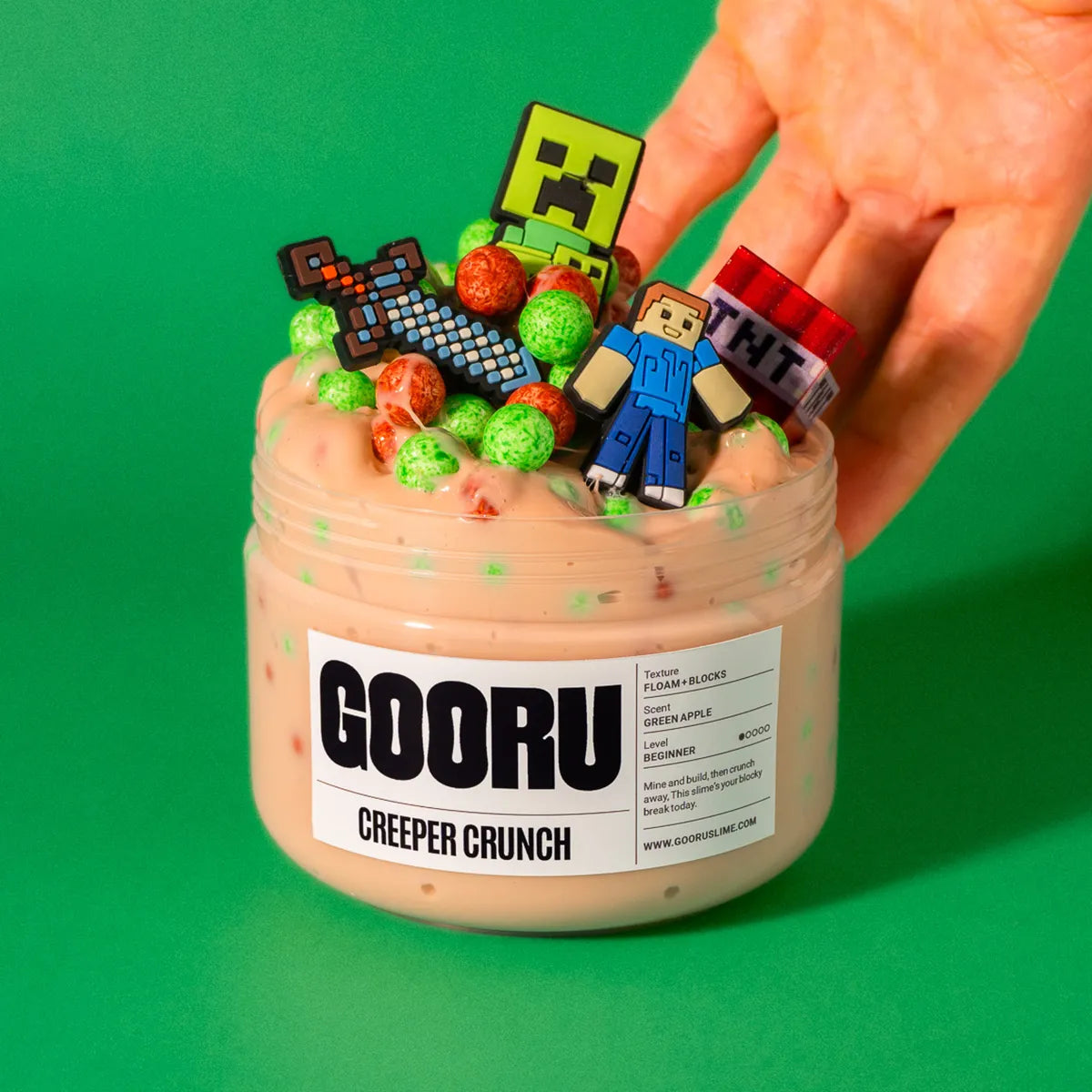 Jar of GOORU Creeper Crunch slime with colorful character figurines on a green background