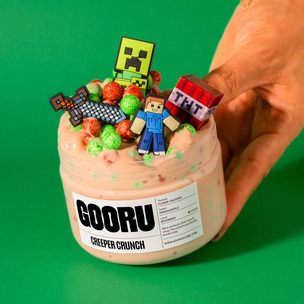 Container of GOORU Creeper Crunch slime with colorful pieces and character figurines on a green background