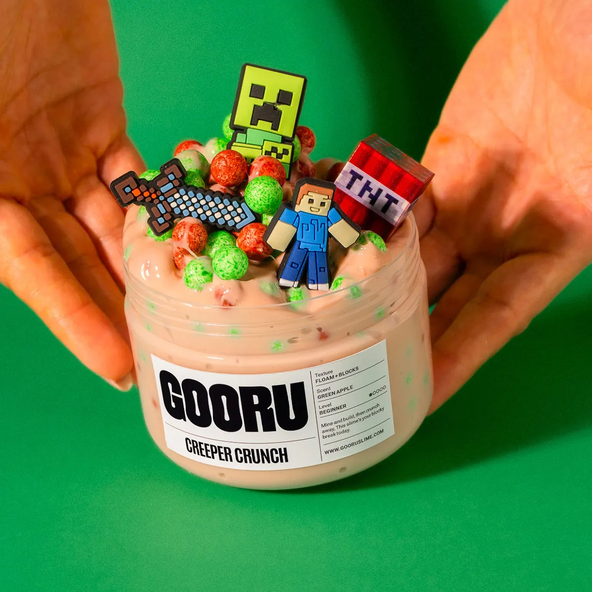 Container of 'GOORU Creeper Crunch'  slime with toy figures on a green background