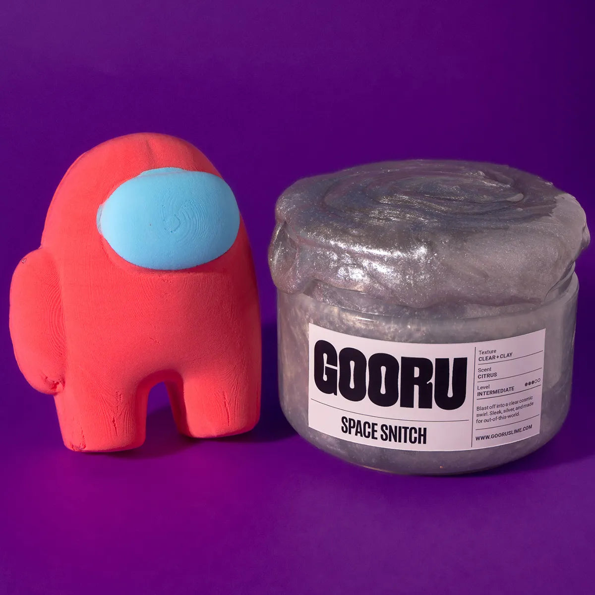 Red character toy next to a jar of GOORU Space Snitch slime on a purple background
