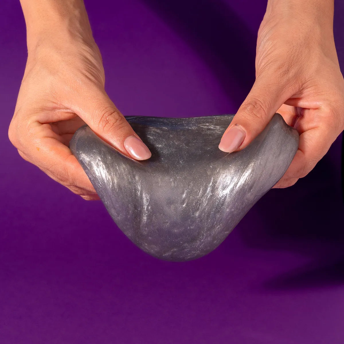 Hands holding gray slime against a purple background