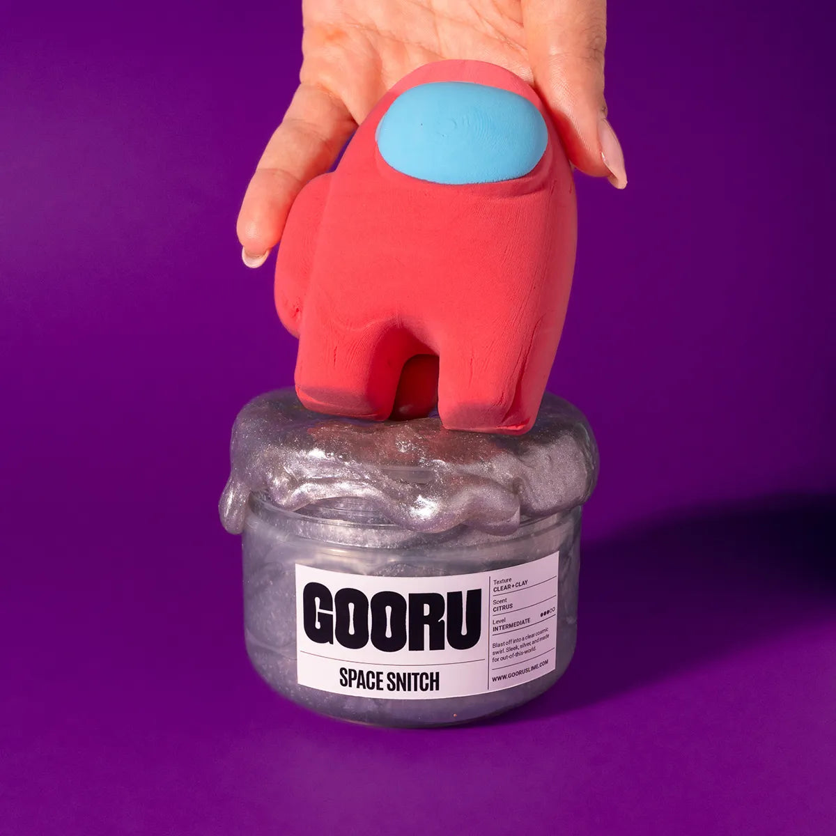 Red and blue toy figure on top of a slime container labeled 'GOORU' against a purple background