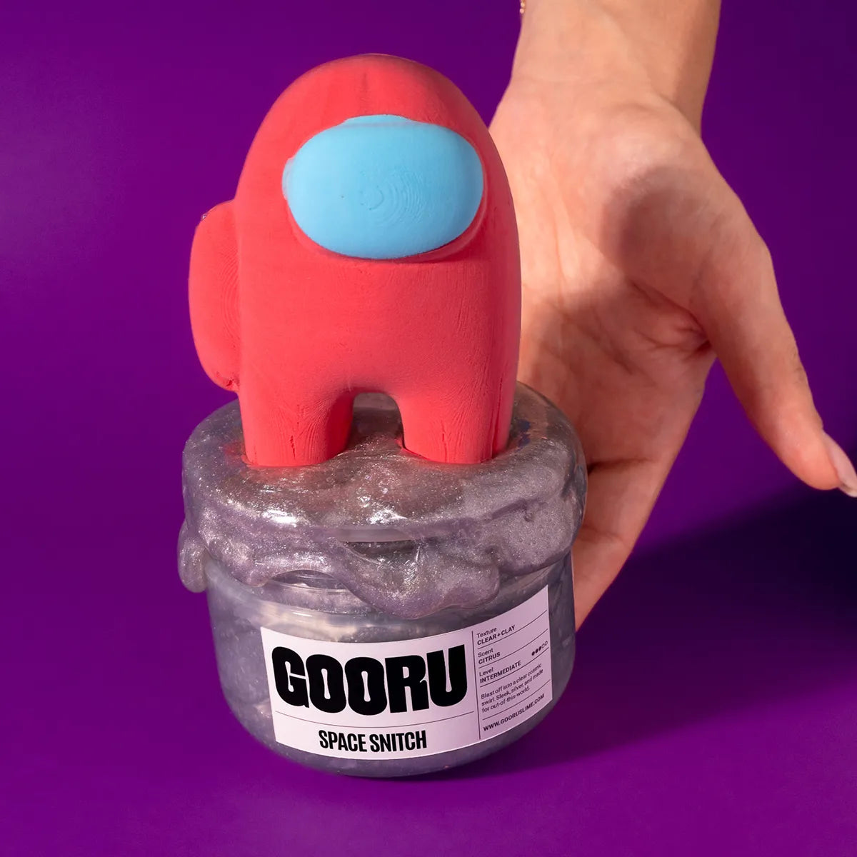 Red and blue toy figure on a GOORU slime container against a purple background