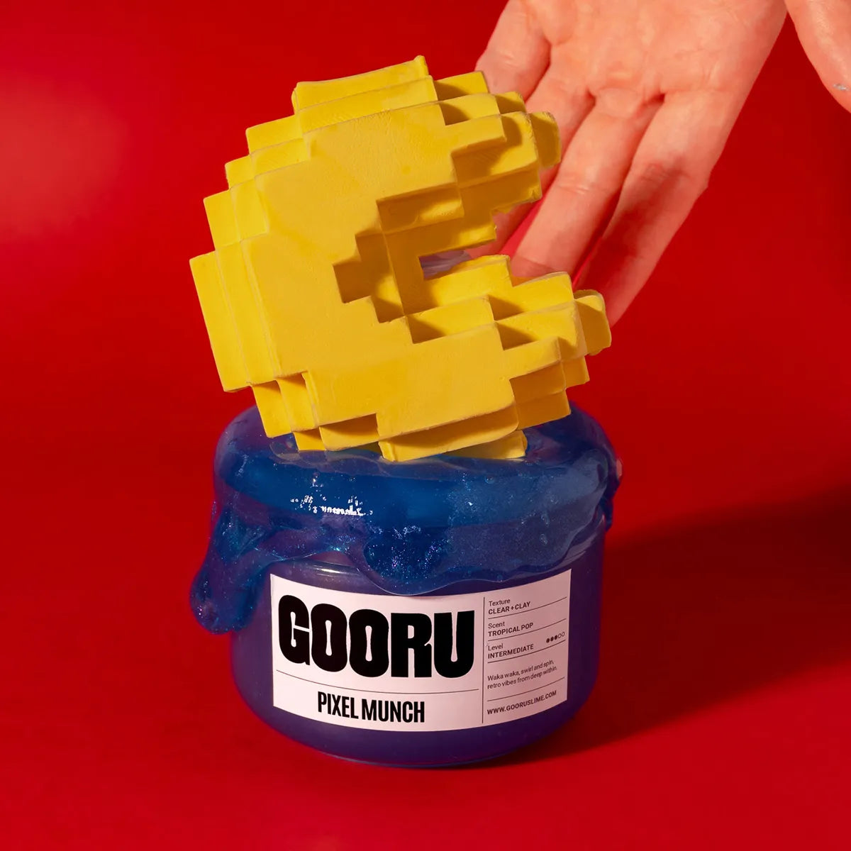 Yellow pixelated object being taken out of a blue slime container labeled 'GOORU Pixel Munch' on a red background.
