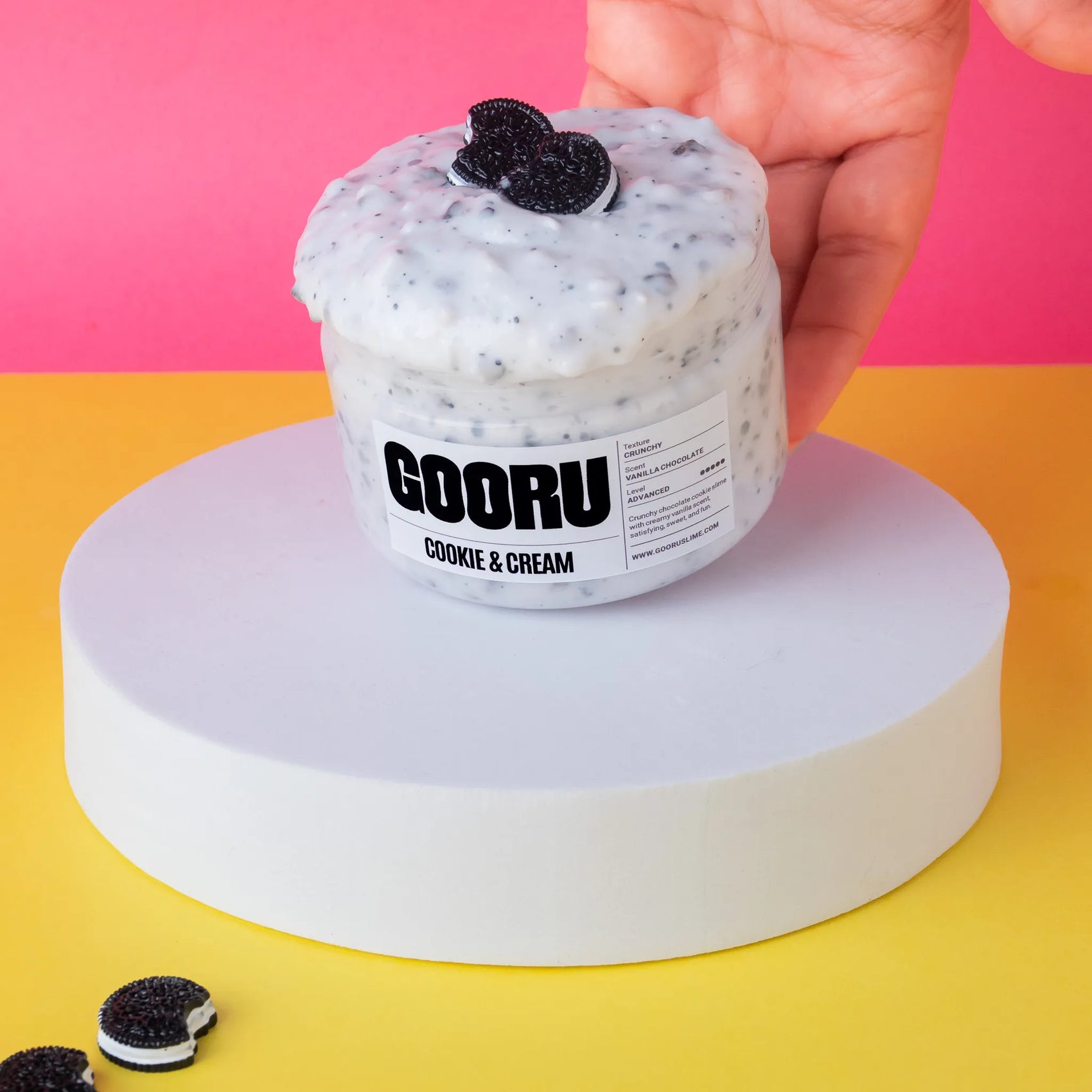 Hand holding a container of GOORU Cookie & Cream slime on a colorful background