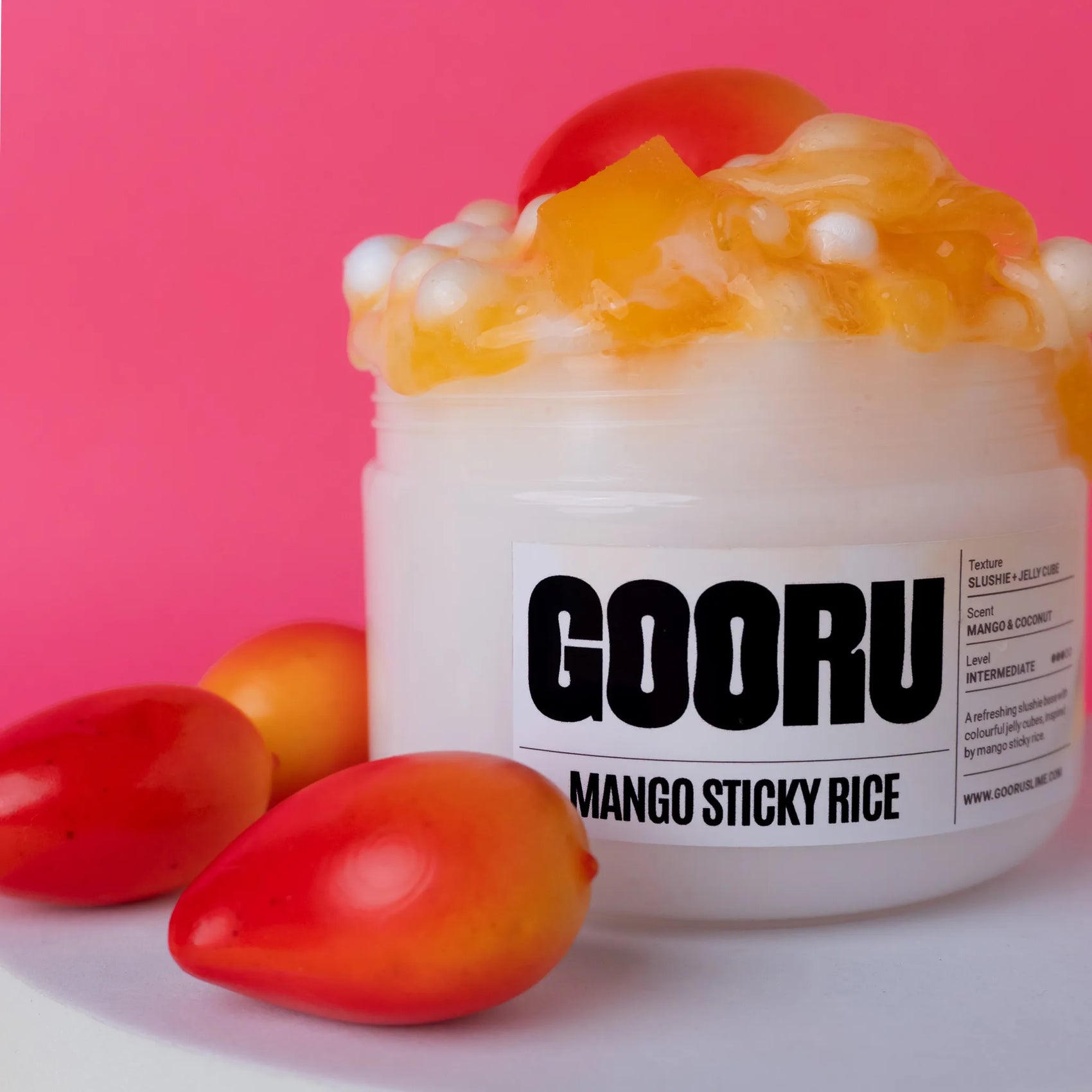Jar of GOORU Mango Sticky Rice slime with mangoes on a pink background