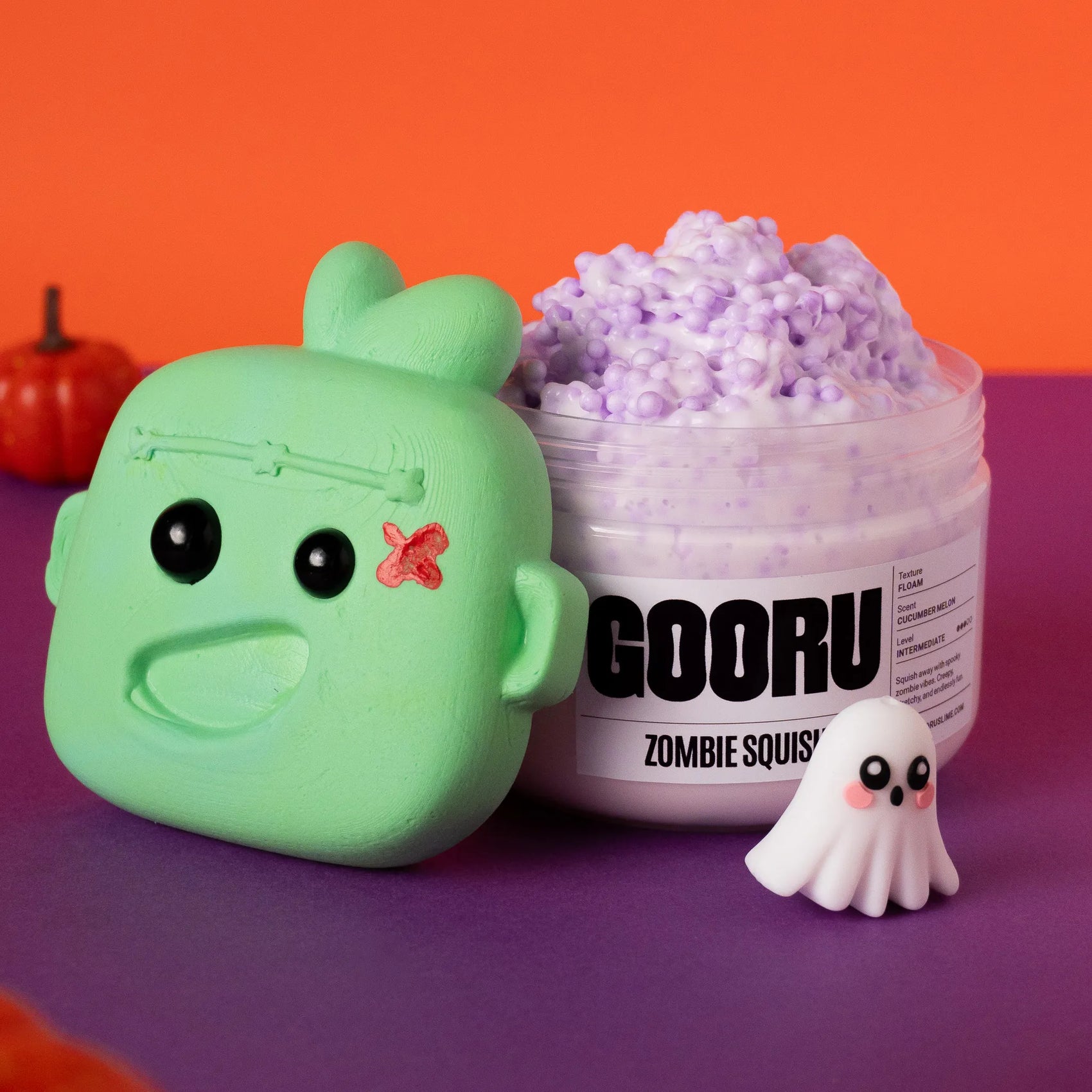 Green zombie-shaped container with a purple substance, labeled 'GOORU Zombie Squish', on an orange and purple background.