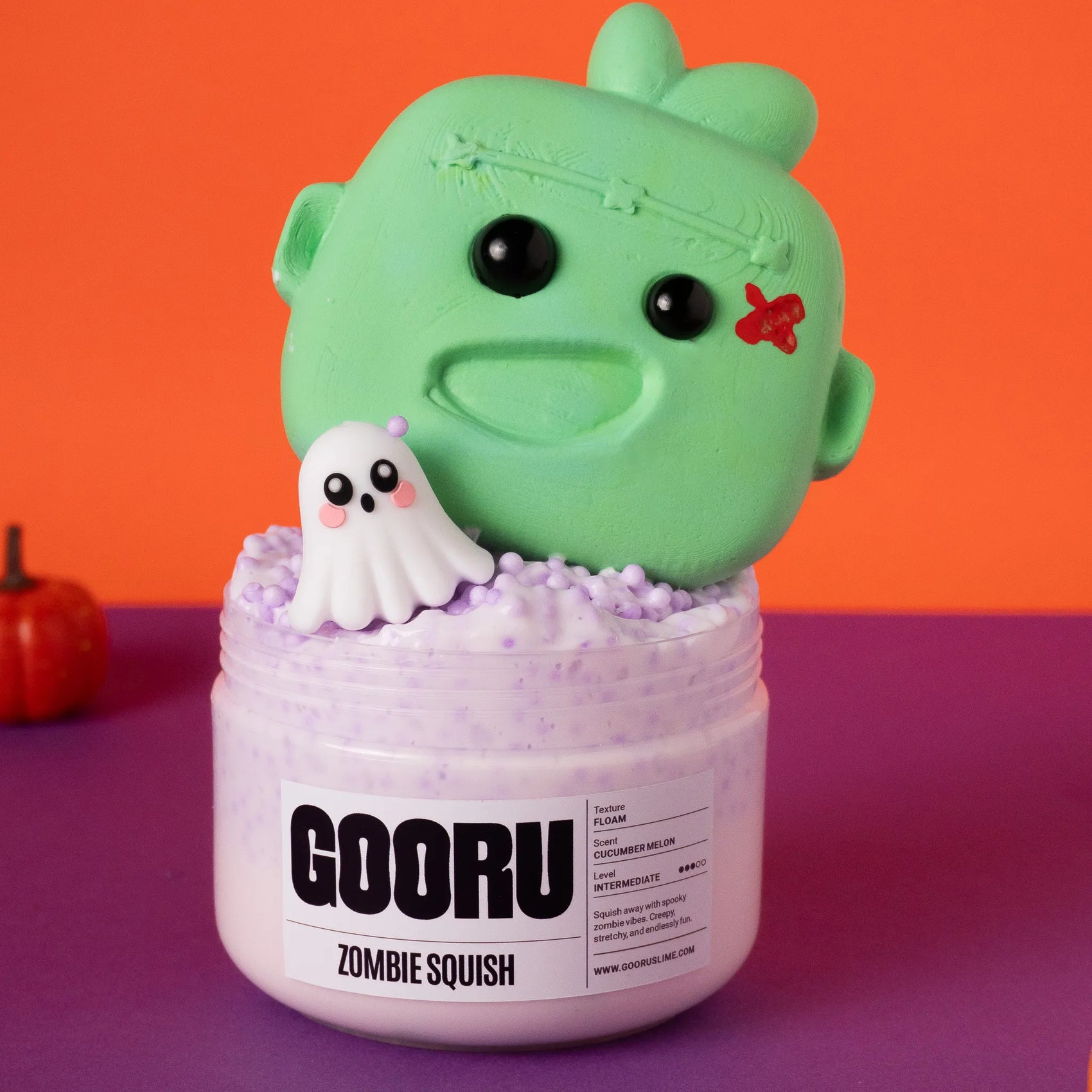 Green zombie squish toy with a ghost on top of a purple container labeled 'GOORU Zombie Squish' against an orange and purple background.