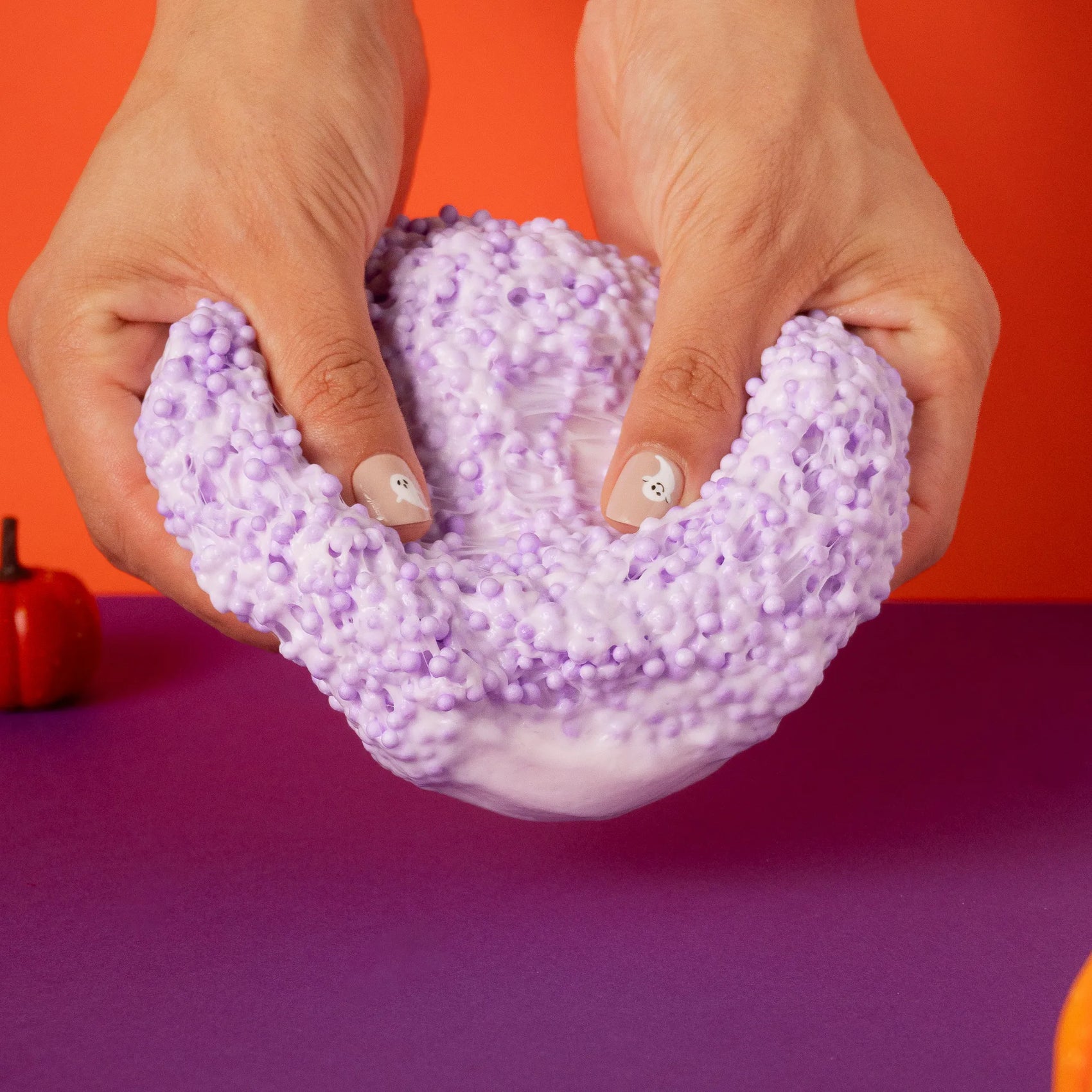 Purple and white textured object held by hands against a red and purple background