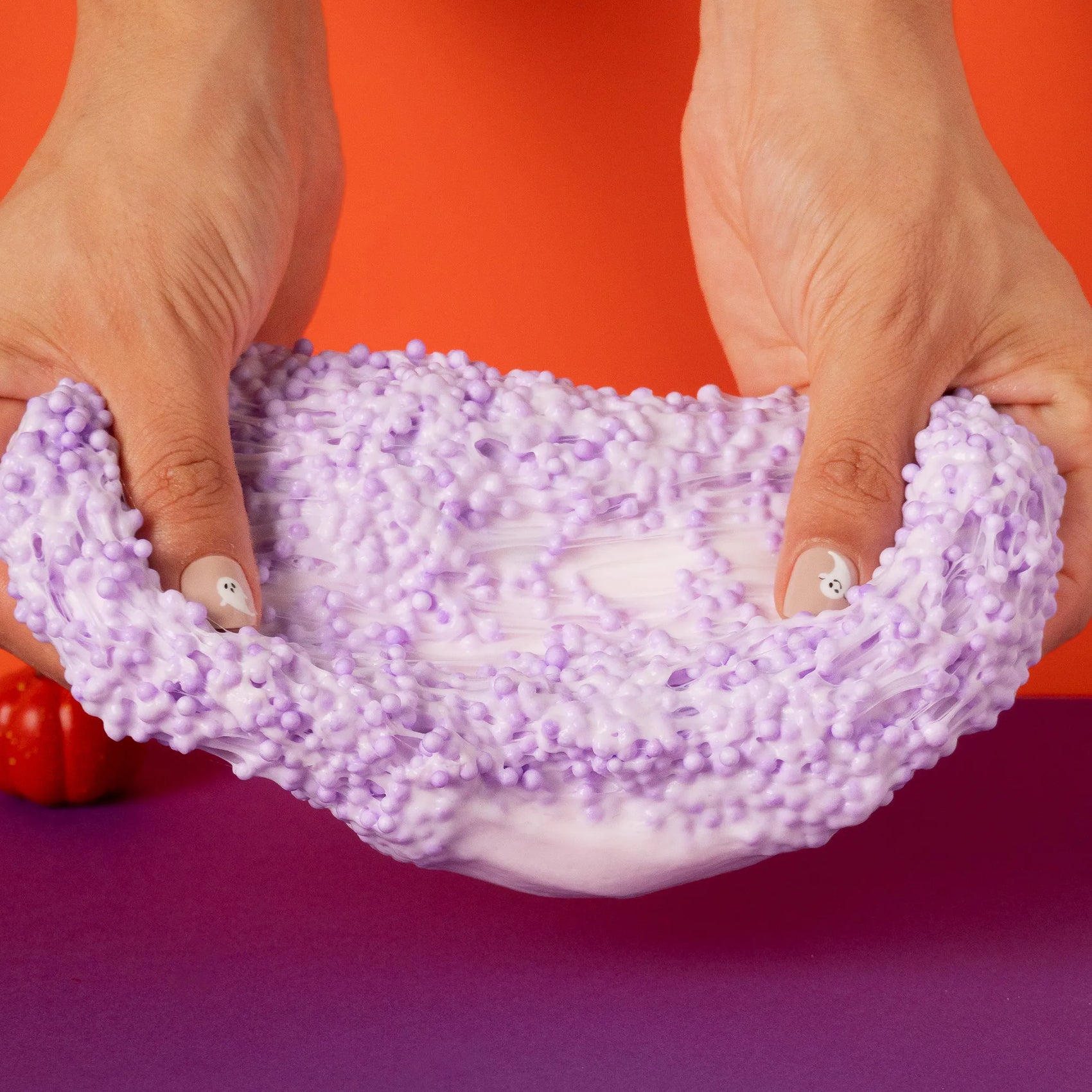 Purple slime with small beads being held by hands against a red and purple background