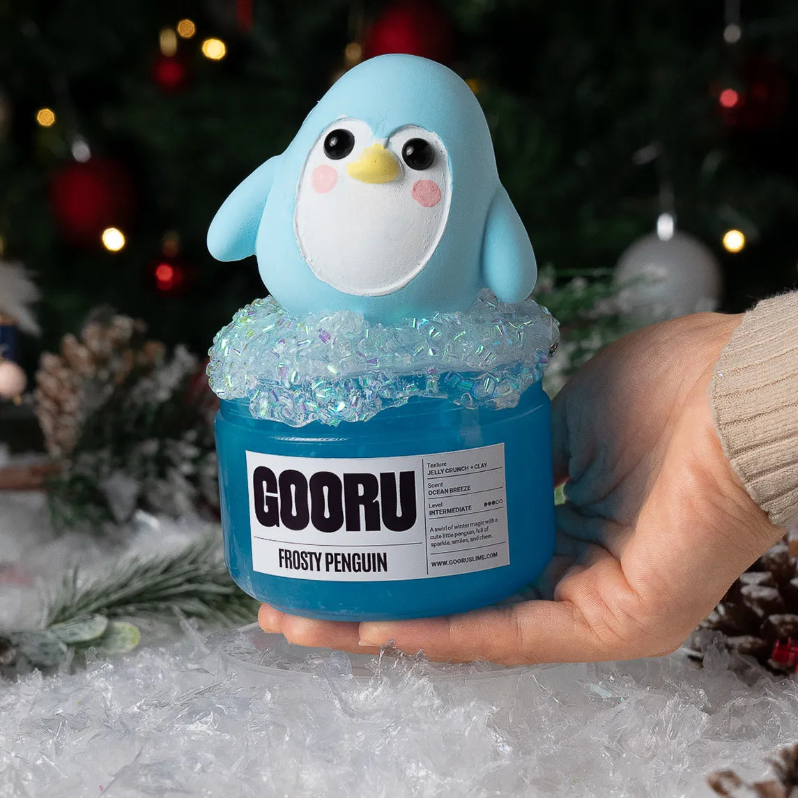 Blue penguin figurine with 'GOORU' label held by a hand against a festive background