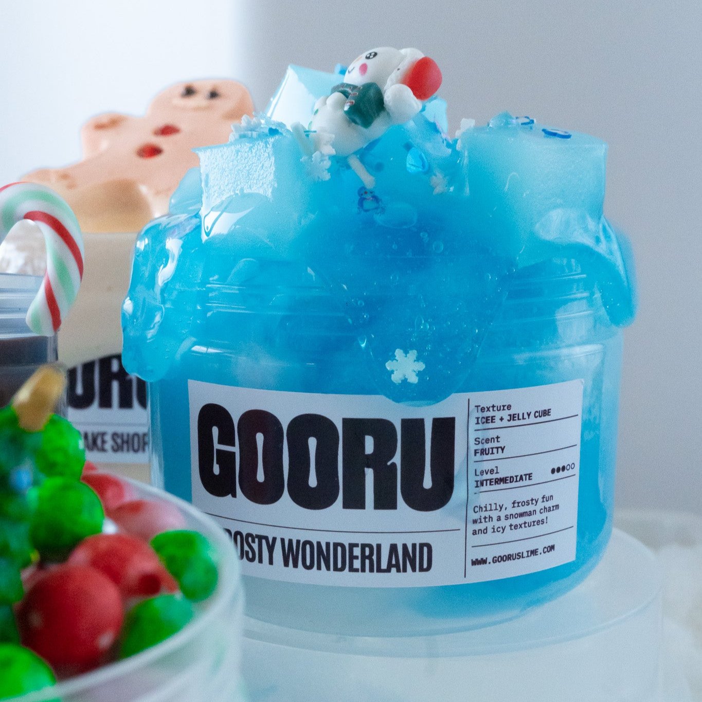 Frosty Wonderland slime displayed with a festive setup, including a gingerbread charm and candy canes in the background. The blue slime, with its icy texture and winter-themed figurine, stands out against the holiday decor.