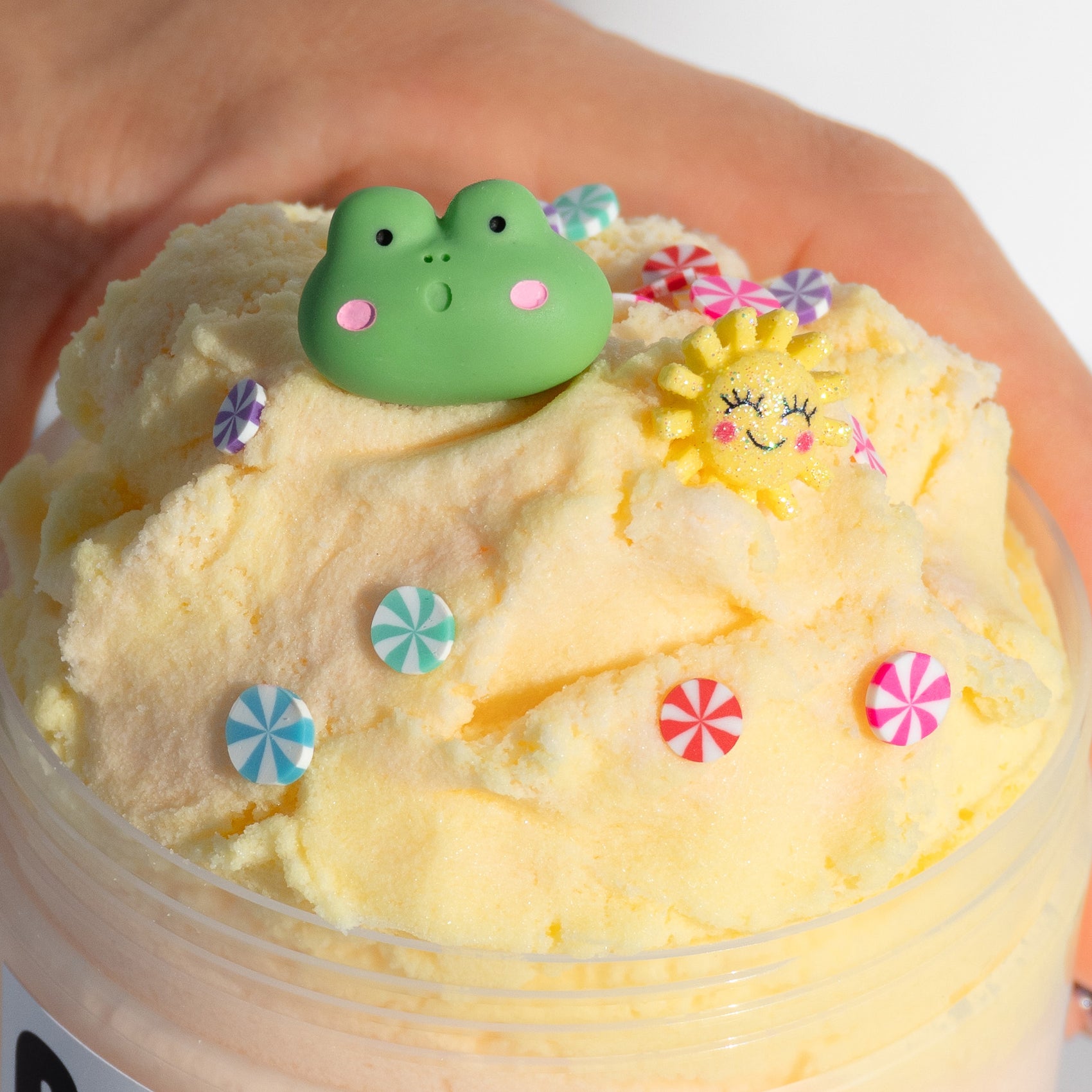 A close-up of Marshmallow Swirl slime, highlighting its fluffy cloud texture and fun charms, including candy pieces, a frog, and a sun.