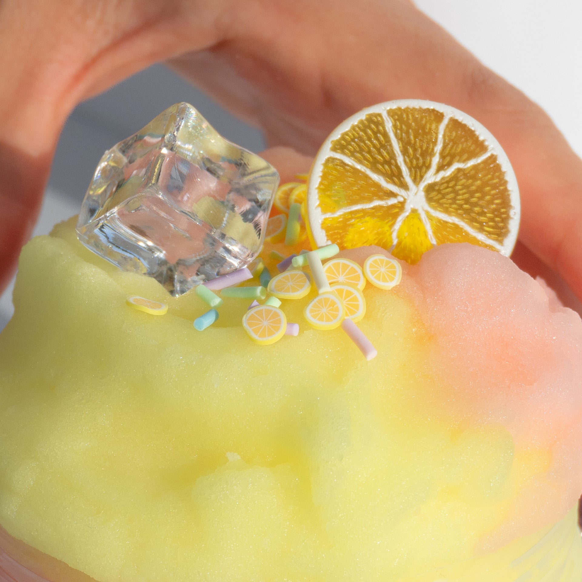 A close-up of the Pink Lemonade slime, featuring vibrant yellow and pink ice textures, adorned with a lemon slice charm and colorful sprinkles.
